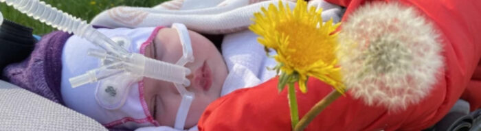 Liegendes Baby mit Sauerstoffversorgung über die Nase. Löwenzahnblüten im Vordergrund.